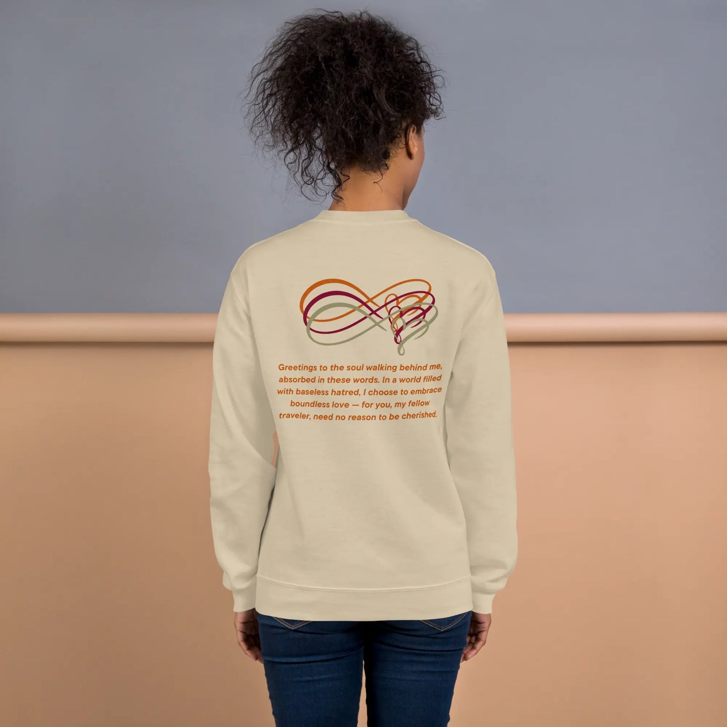 Person wearing a beige sweatshirt with an infinity symbol design and text on the back, standing against a plain background.